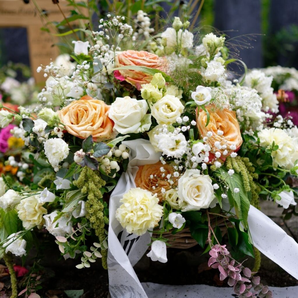 Composition florale élaborée avec roses pêche, fleurs blanches et feuillage, déposée sur une sépulture en Essonne