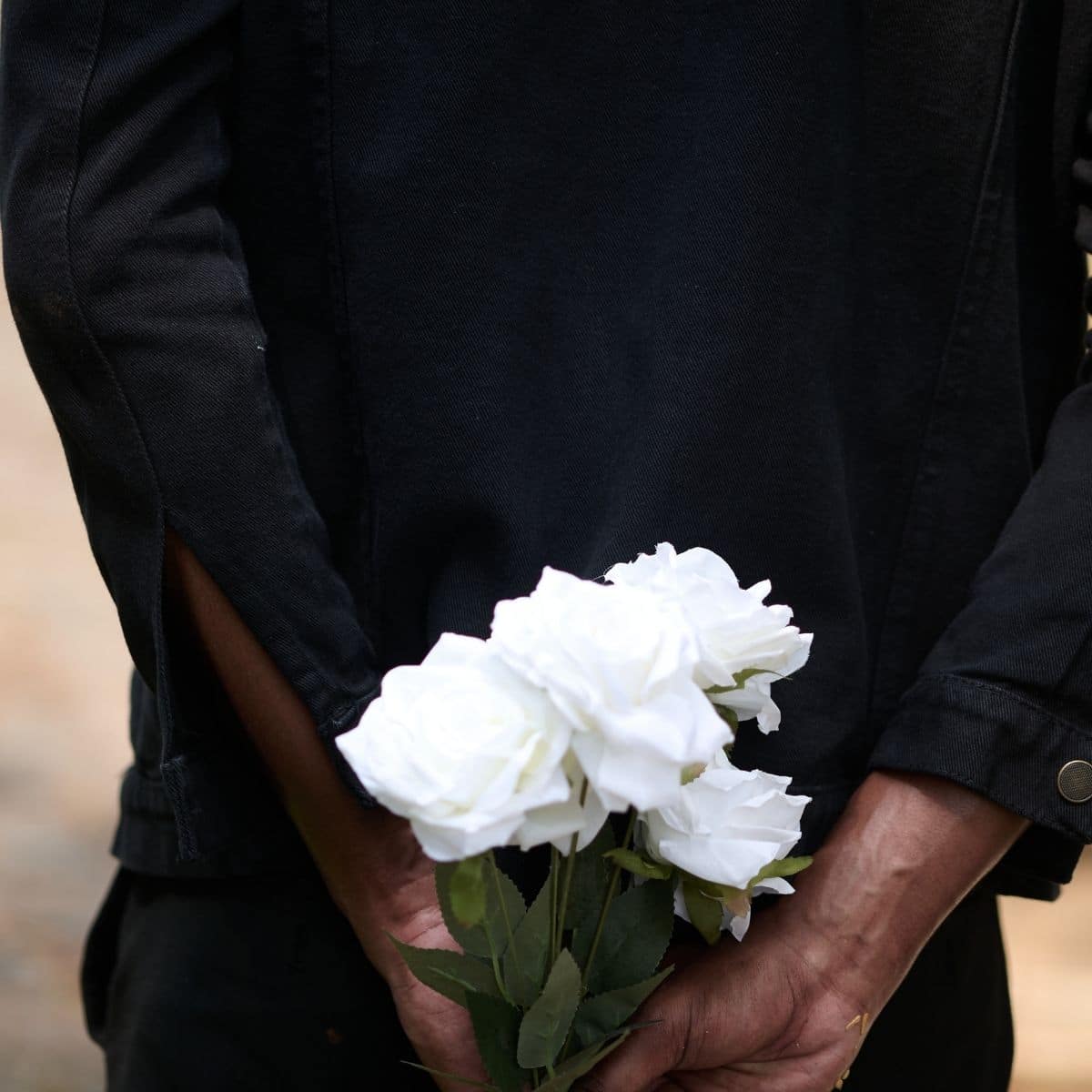 Personne vêtue de noir tenant un bouquet de fleurs blanches, dans un contexte de recueillement