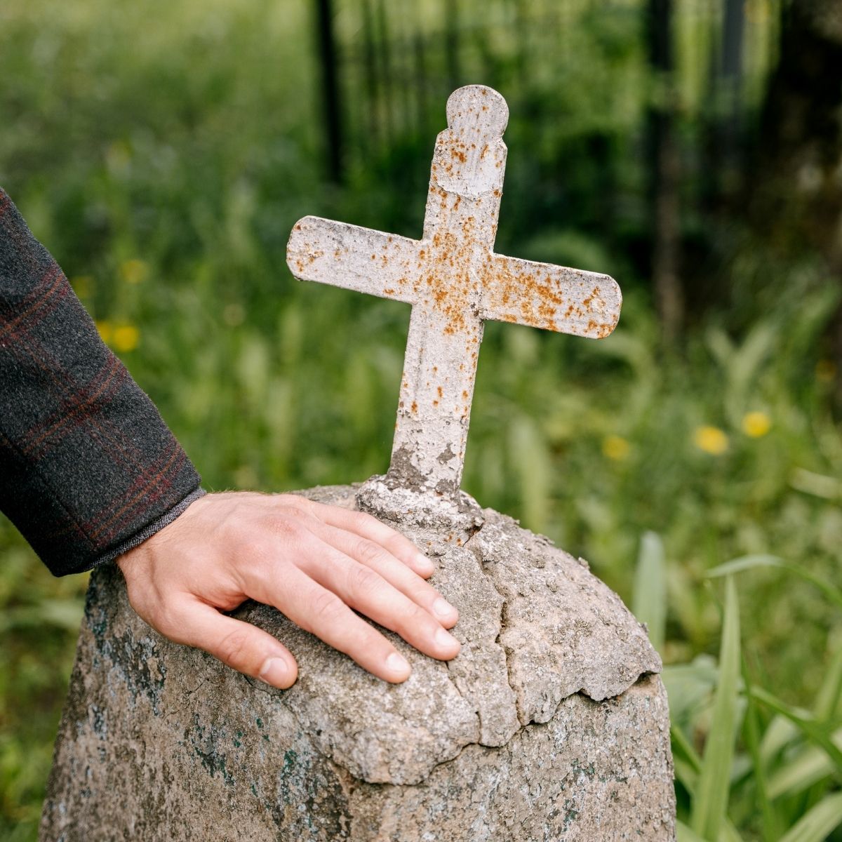 Main posée avec soin sur une croix en pierre ancienne dans un cimetière