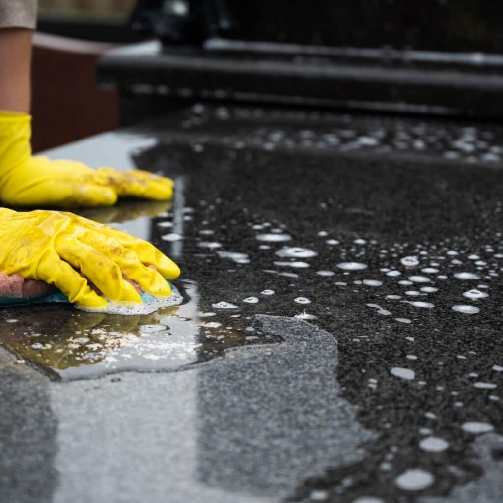 Mains gantées de jaune nettoyant une pierre tombale en granit avec une éponge humide